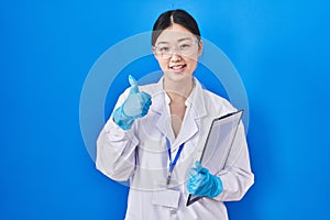 Chinese young woman working at scientist laboratory doing happy thumbs up gesture with hand
