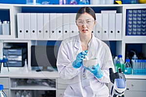 Chinese young woman working at scientist laboratory mixing clueless and confused expression