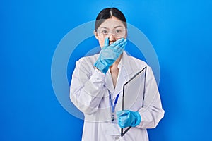 Chinese young woman working at scientist laboratory shocked covering mouth with hands for mistake