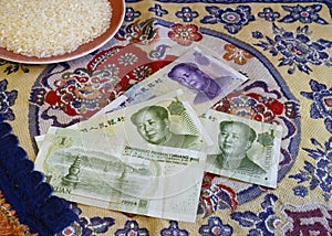 Chinese yuan banknotes and a cup of rice on the background of national embroidery