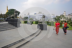Chinthe Statues in Yangon Myanmar with beautiful women in Red in front & temple & colonial buildings in the background
