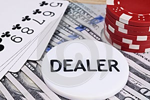 Chip `Dealer` lies on the background of hundred-dollar bills and gaming poker cards