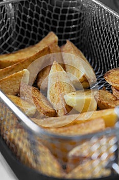 Chips cooking in vegetable oil in a deep fat fryer appliance.  Unhealthy fast food concept
