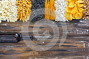 Chips, crackers, seeds, nuts and bottle of fresh cold beer on wooden table