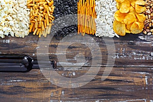 Chips, crackers, seeds, nuts and bottle of fresh cold beer on wooden table