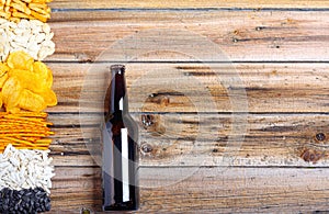 Chips, crackers, seeds, nuts and bottle of fresh cold beer on wooden table