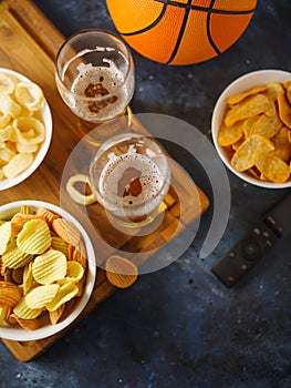 Chips, onion rings, snacks, beer in two glasses and a remote control. Dark blue background. View from above. Watching your