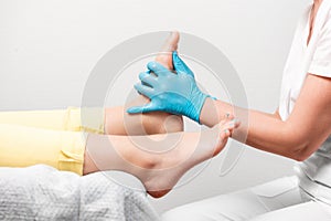 A chiropodist massages the feet of client. Close-up of legs and master& x27;s hands in blue medical gloves. The concept