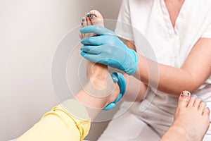 A chiropodist massages the feet of client. Close-up of legs and toenails with titanium thread. The concept of pedicure