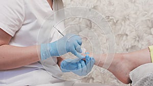 Chiropodist in medical gloves cleaning the toenails with a double-sided curette. Close up, side view. The concept of