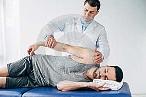 Chiropractor stretching arm of handsome patient lying on massage table