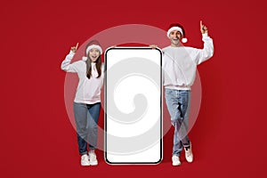 Chistmas Idea Concept. Couple In Santa Hats Standing With Big Blank Smartphone