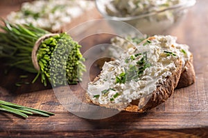 Chive cream cheese spread on a bread slice next to bunch of freshly cut chives and a bowl of spread in the background