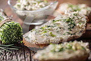 Chive cream cheese spread on a bread slice next to bunch of freshly cut chives and a bowl of spread in the background