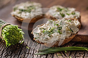 Pažitka smetanový sýr pomazánka na plátky chleba vedle banda čerstvě nakrájené pažitky na rustikální dřevo a prkénko
