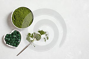 Chlorella green powder and spirulina pills on a white concrete background. Natural mineral dietary supplements for health. Copy