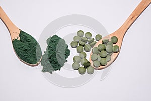 Chlorella tablets and spirulina powder on two wooden spoons
