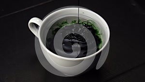 Chlorophyll extract is poured and mixed with pure water in a white cup against a dark background.