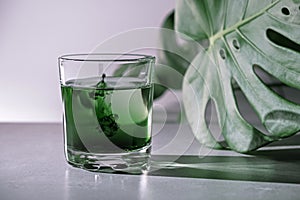 Chlorophyll extract is poured in pure water in glass against a white grey background with green leaf