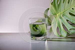 Chlorophyll extract is poured in pure water in glass against a white grey background with green leaf