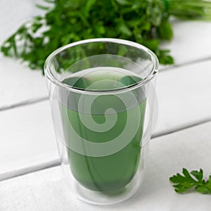 Chlorophyll water in a glass cup with green leaves on white wooden table