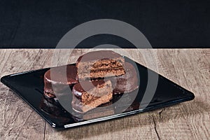 Chocolate alfajor on black plate on a wooden table and dark background