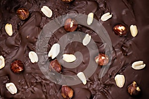 Chocolate background with peanuts and hazelnuts close-up, top view