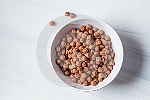 Chocolate balls corn flakes in white bowl, white background. Breakfast food concept