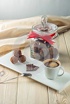 Chocolate balls truffles on a saucer next to a jar of candy and a Cup of coffee. The concept of delicious desserts gifts