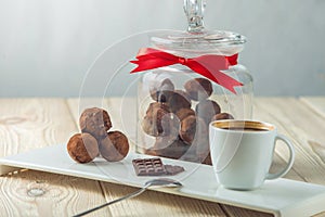 Chocolate balls truffles on a saucer next to a jar of candy and a Cup of coffee. The concept of delicious desserts gifts