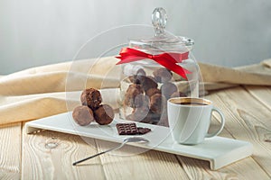 Chocolate balls truffles on a saucer next to a jar of candy and a Cup of coffee. The concept of delicious desserts gifts