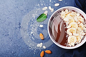 Chocolate banana almond coconut smoothie bowl on stone table top view. Healthy and diet breakfast or dessert. Flat lay.