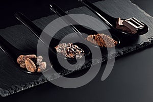 Chocolate bar, cocoa powder, cacao beans and nibs, heap in wooden spoons, chocolate background