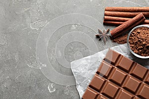 Chocolate bar and cocoa powder on grey, flat lay. Space for text