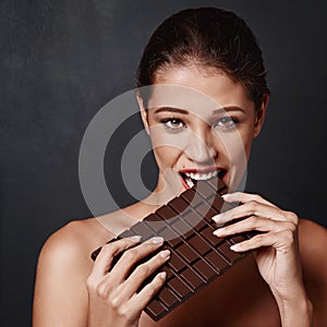 Chocolate bar, portrait and woman in studio eating for unhealthy diet, craving sugar or cheat day on dark background