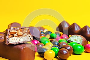 Chocolate bars, colorful candies, sweets on a yellow background