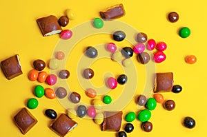 Chocolate bars, colorful candies, sweets on a yellow background, top view