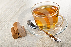 Chocolate bars, cup with hot tea, spoon on saucer on wooden table