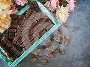 Chocolate bars in a vintage box. Chocolate beans,  flowers,pieces of chocolate scattered on a textural background