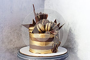 Chocolate birthday cake with golden stripes, dark chocolate decoration and macaroons