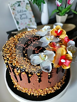 Chocolate birthday cake with peanuts topping and flowery decoration.