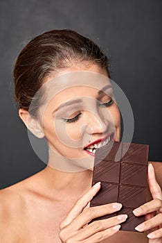 Chocolate, bite and woman in studio eating for unhealthy diet, sugar craving or cheat day on dark background. Dessert