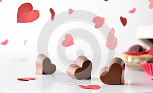 Chocolate bonbons on white table and heart cutouts falling down