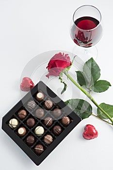 Chocolate box, roses and red wine glass on white background