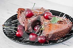 Chocolate brownie on a black plate sprinkled with cherries.