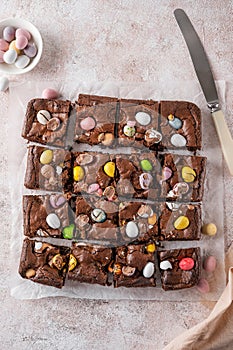 Chocolate brownie with Easter candies in the form of colored eggs with a bottle of milk. Easter dessert. Copy space
