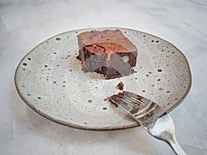 Chocolate brownie and a fork on a plate, already eaten or tasted.