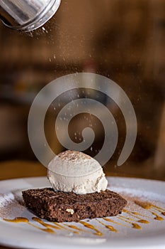 Chocolate brownie with ice cream in a plate with rain of icing sugar