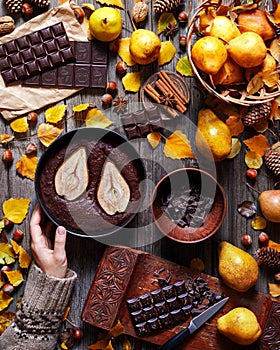 Chocolate Brownie with a pear in a baking dish is held by a female hand in a sweater. Food gathering, style. Autumn