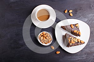 Chocolate cake with caramel, peanuts and almonds on a black wooden background